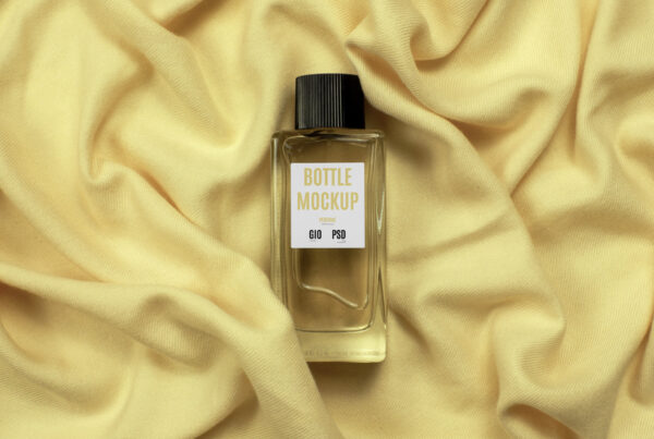 Seen from above, small Glass Bottle Perfume Mockup with paper label laying on bright yellow blanket.