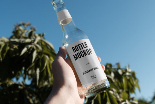Raised hand with an Open Glass Bottle Mockup in hand against the blue sky and Citrus Sinensis.