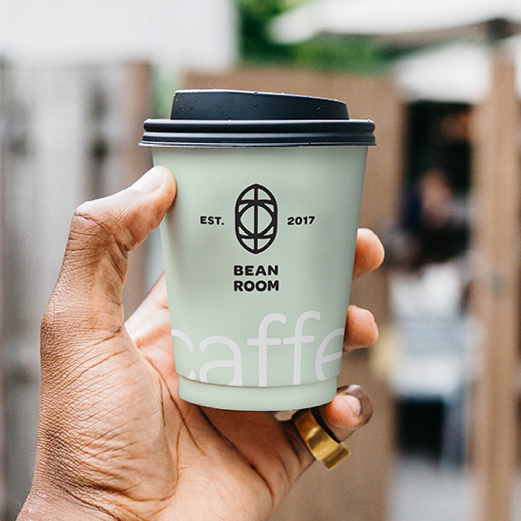 A Small Cup Mockup in men left hand against café.