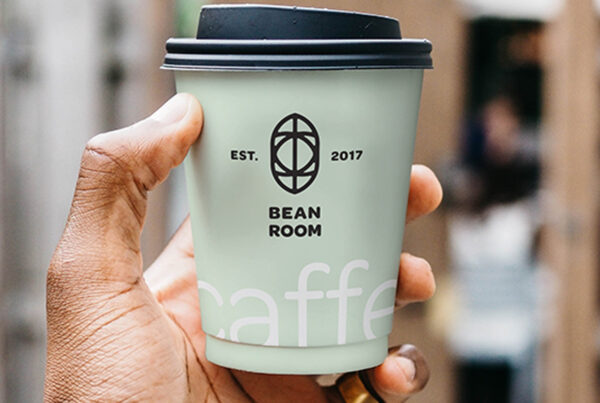 A Small Cup Mockup in men left hand against café.