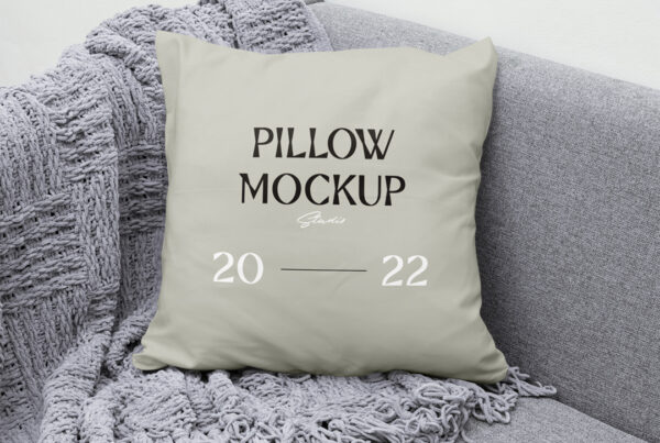 Front view Pillow Mockup lies on gray couch with gray blanket.