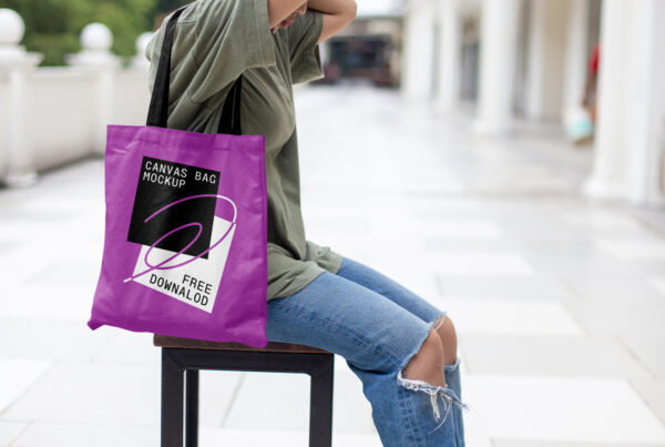Women sitting on a wood chair wearing a canvas bag mockup on her shoulder.