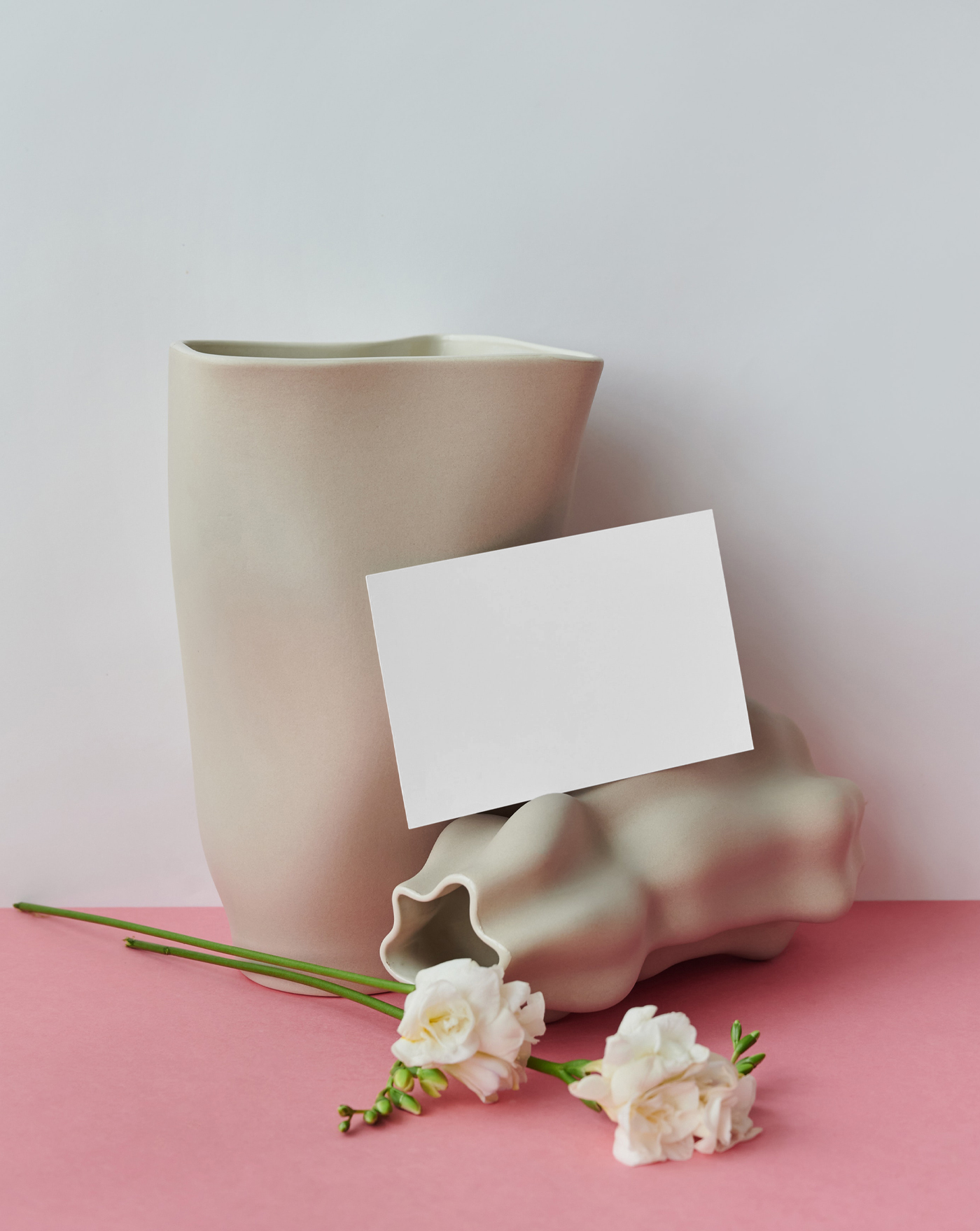 The blank card mockup is placed on the table with flowers and vases seen from the front.