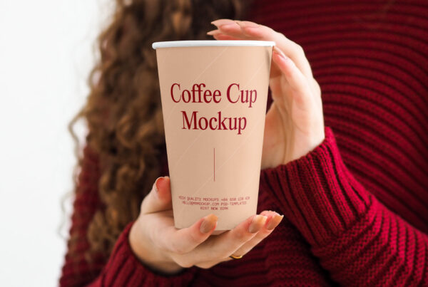Woman in red sweater holding a paper coffee cup mockup in her hands.