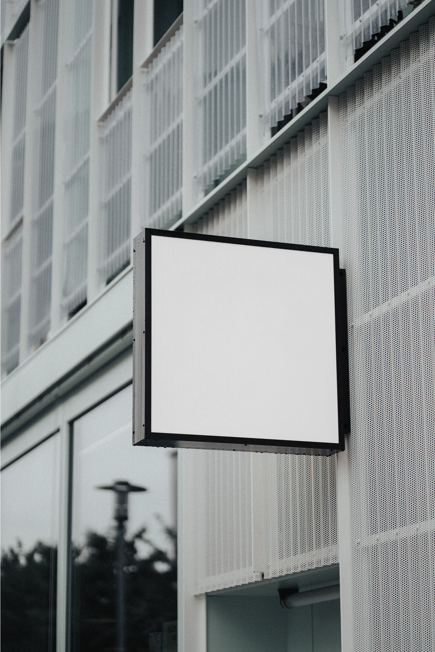 A Blank Square Sign Mockup is hanging attached to the building.