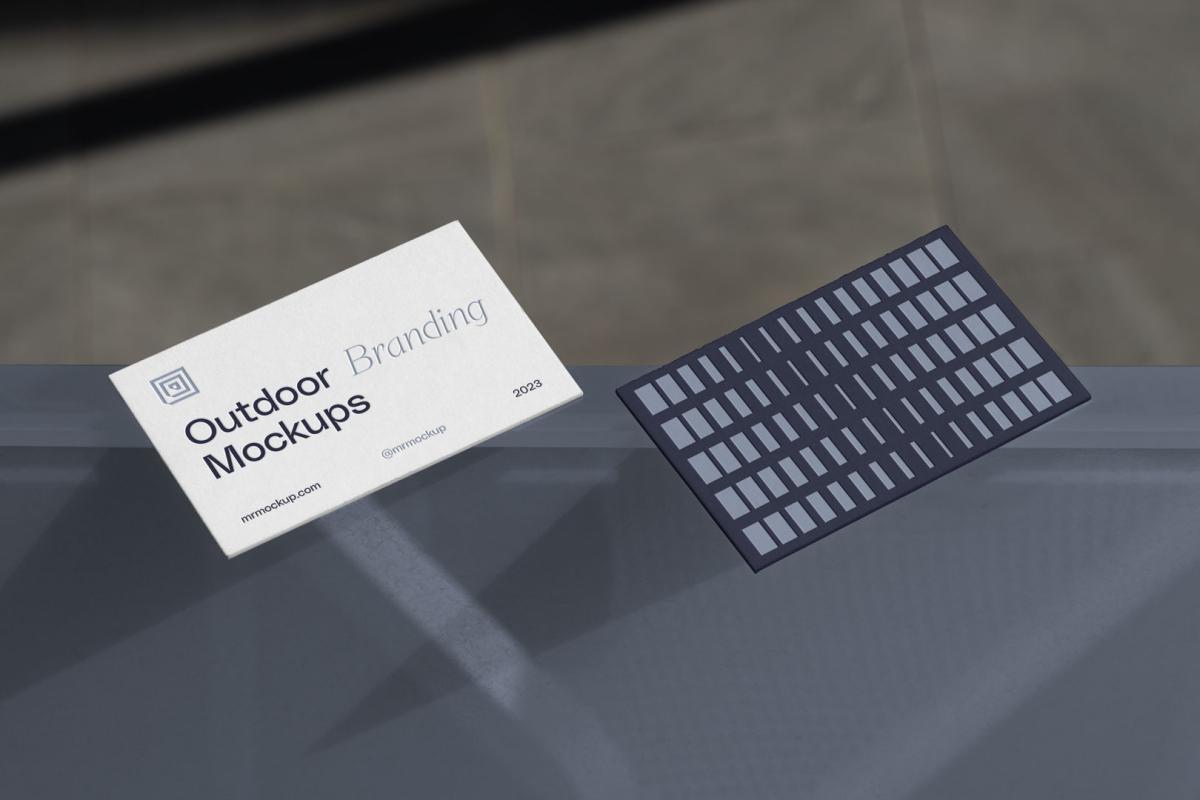 Two business cards laying on the blue glass from outdoor branding mockups.