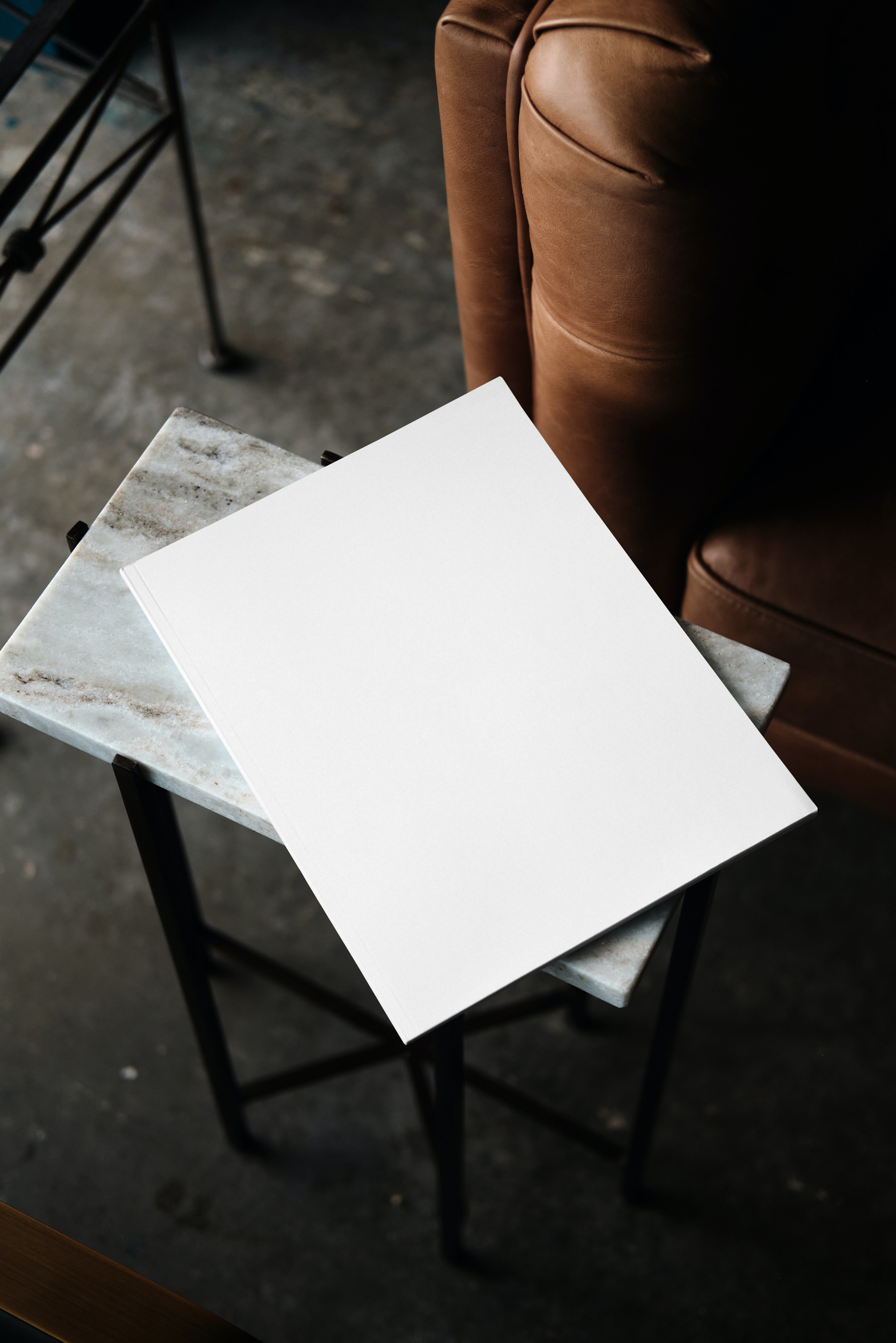 Free Blank Magazine Mockup laying on the marble table near leather armchair in modern flat.