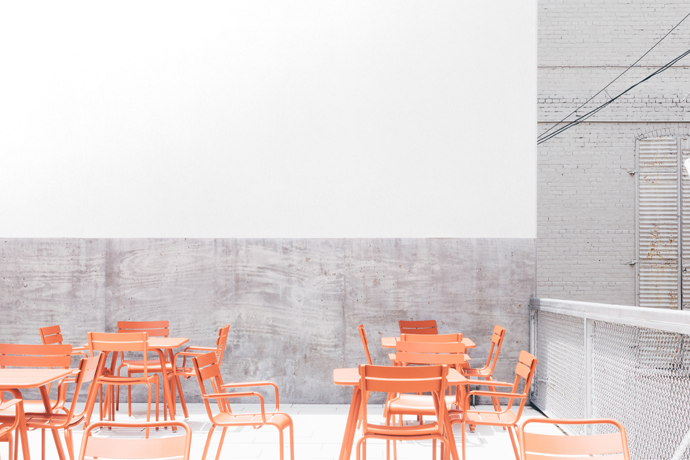 Free White Restaurant Wall Mockup seen from front with metal chairs in restaurant garden.