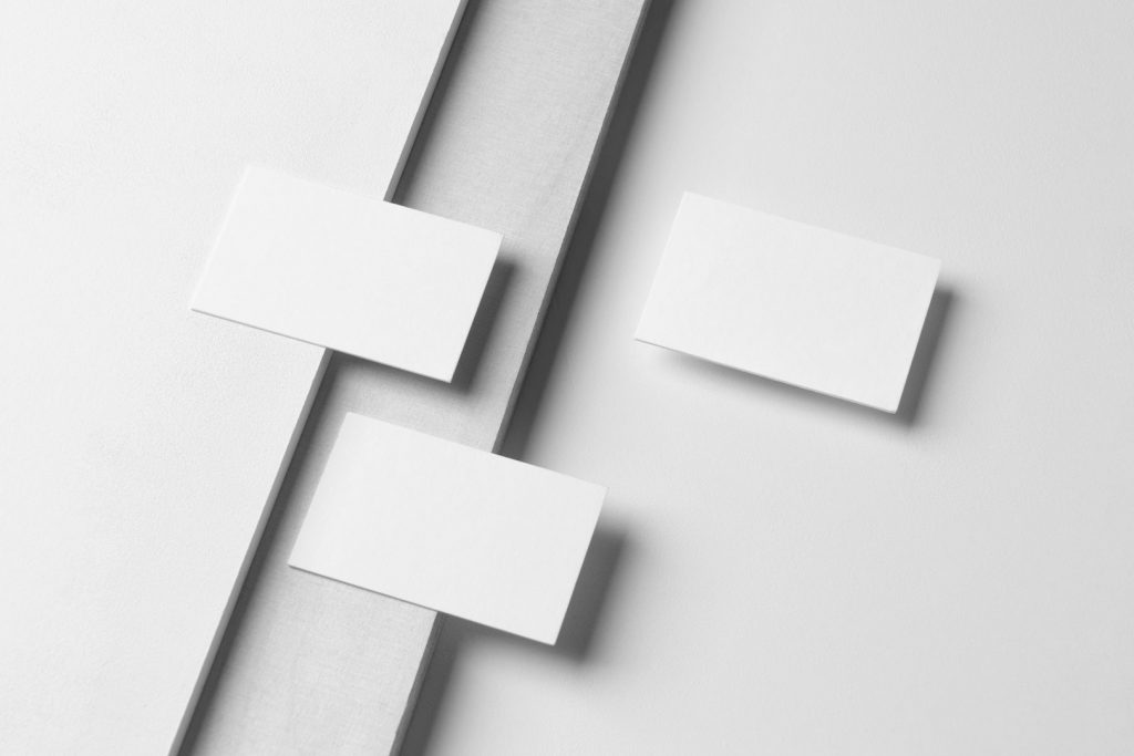 Three White Business Cards Branding Mockups seen from the above laying on white boxes and white wood texture.