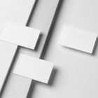 Three White Business Cards Branding Mockups seen from the above laying on white boxes and white wood texture.