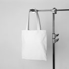 Seen from the front, White Canvas Bag Branding Mockup hanging on a tripod on at white background.