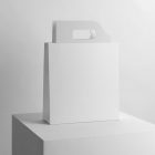 White Paper Bag with Handle Branding Mockup standing on the white cubic against a white wall.