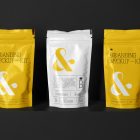 Three Coffee Bags Branding Mockups Kit with yellow design seen from the front is standing located on the black wooden stairs.