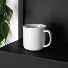 A White Metal Mug Branding Mockups Kit seen from above is standing on the black wooden stairs.