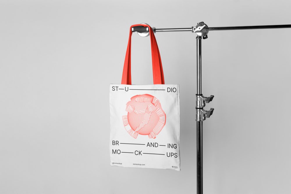Seen from the front Canvas Bag Branding Mockup hanging on a tripod at light gray background.