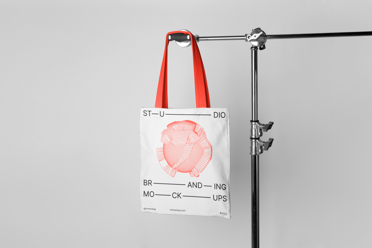 Seen from the front Canvas Bag Branding Mockup hanging on a tripod at light gray background.