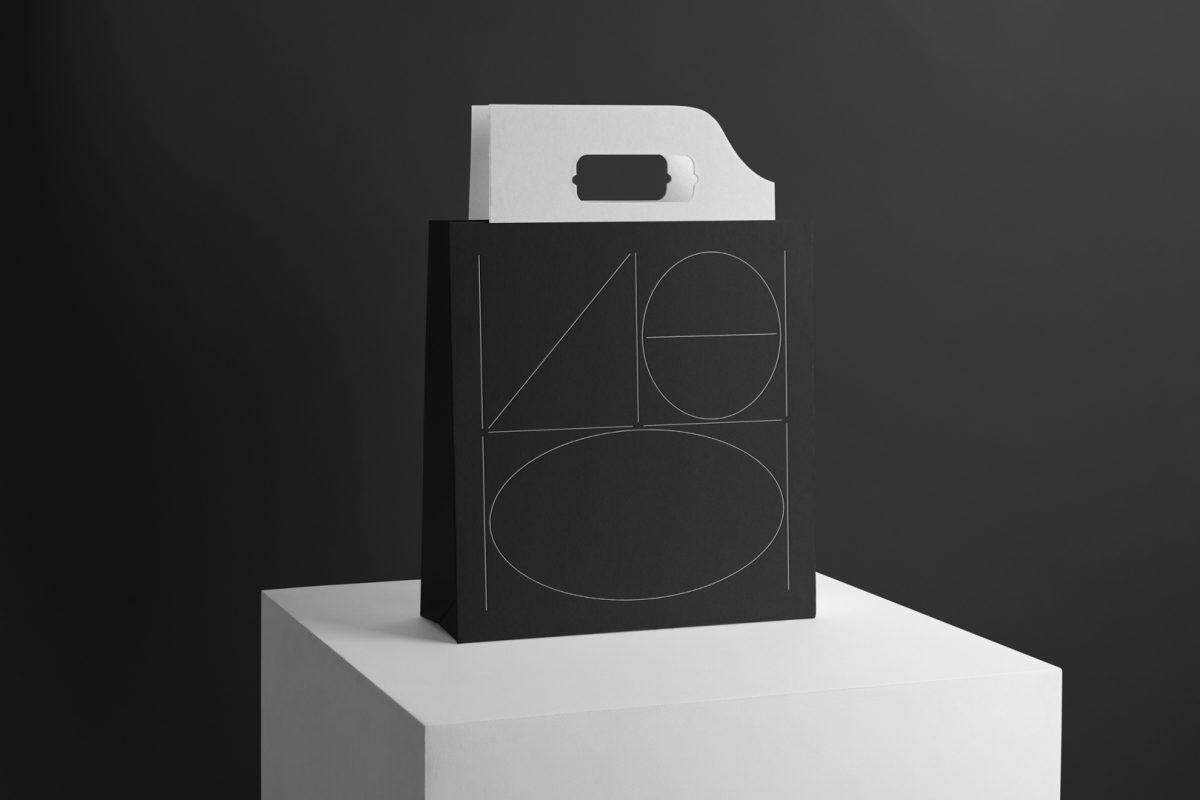 Black Paper Bag with Handle Branding Mockup with a minimalistic design standing on the white cubic on black background.