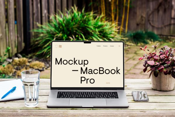 Free front view MacBook Pro Mockup standing on the wood desk against a backyard garden in the background.