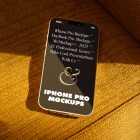 Seen from above, gold iPhone 14 Pro Mockup with black design laying on the reddish yellow couch.