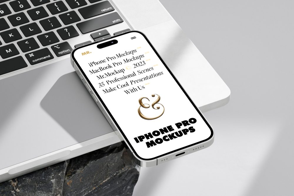 Seen from above, iPhone 14 Pro Mockup with white design laying on the MacBook standing on the big rock against a bright gray background.