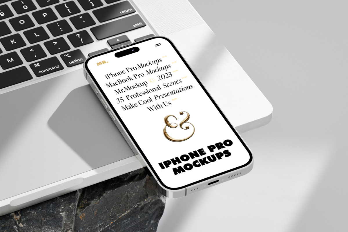 Seen from above, iPhone 14 Pro Mockup with white design laying on the MacBook standing on the big rock against a bright gray background.