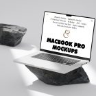 Front view, MacBook Pro Mockup with white design standing on the big piece of rock laying on the bright gray floor against second gray/black rock and gray wall in the background.