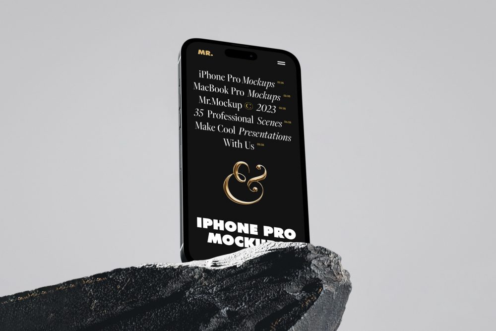 Seen from below, the iPhone 14 Pro Mockup with black design standing on the big rock against the gray wall in the background.