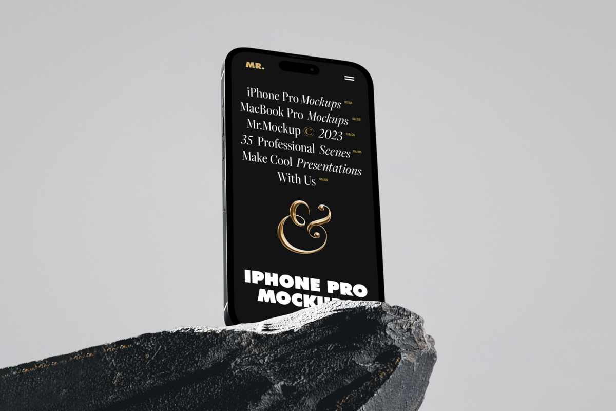 Seen from below, the iPhone 14 Pro Mockup with black design standing on the big rock against the gray wall in the background.