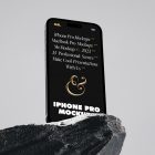 Seen from below, the iPhone 14 Pro Mockup with black design standing on the big rock against the gray wall in the background.