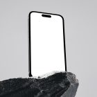 Seen from below, the blank iPhone 14 Pro Mockup standing on the big rock against the gray wall in the background.