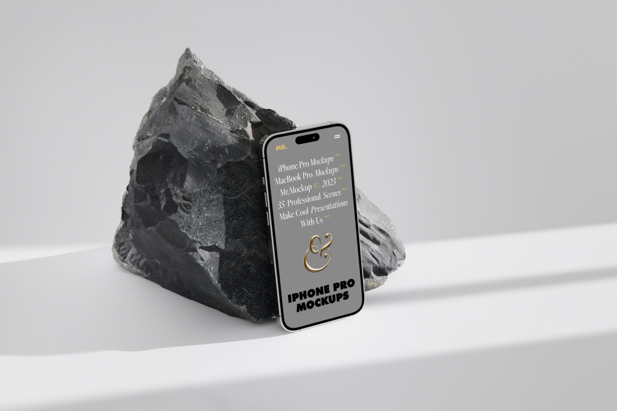 Seen from above, the iPhone 14 Pro Mockup with gray design based on the big piece of rock standing on the bright gray floor.
