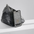 Seen from above, the iPhone 14 Pro Mockup with gray design based on the big piece of rock standing on the bright gray floor.