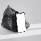 Seen from above, blank iPhone 14 Pro Mockup based on the big piece of rock standing on the bright gray floor.