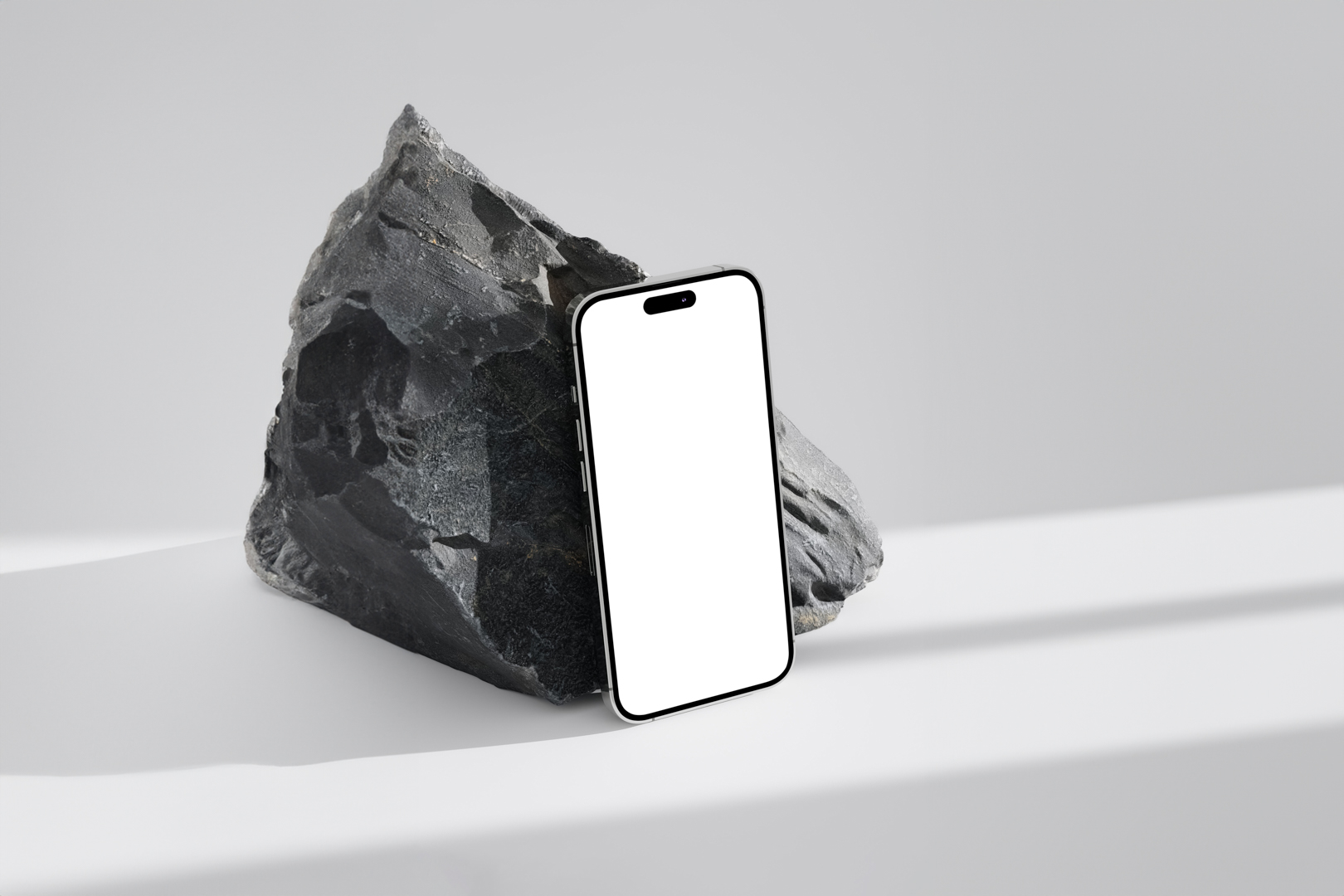 Seen from above, blank iPhone 14 Pro Mockup based on the big piece of rock standing on the bright gray floor.