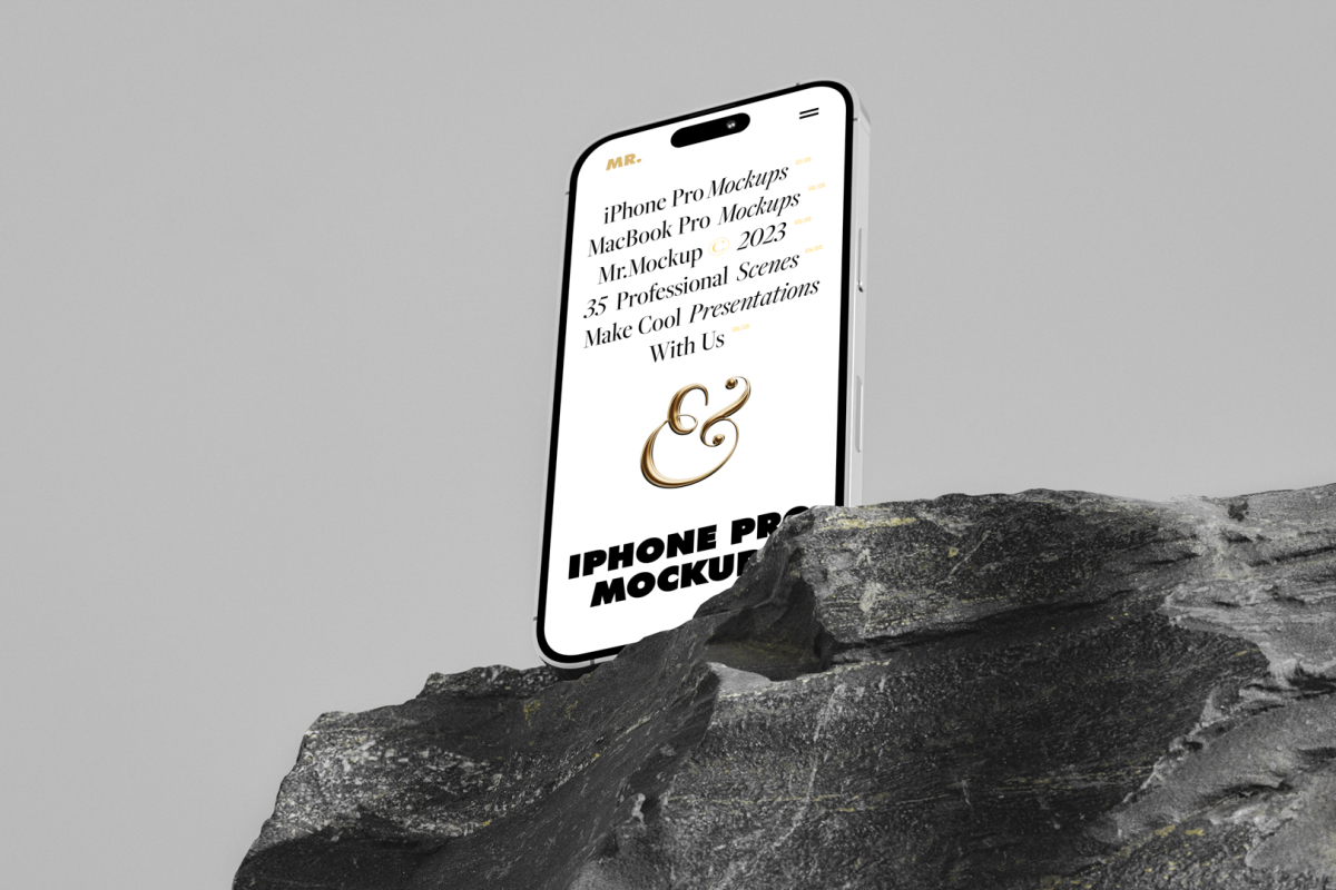 Seen from below, the iPhone 14 Pro Mockup with white design standing on the big rock against the gray wall in the background.