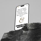 Seen from below, the iPhone 14 Pro Mockup with white design standing on the big rock against the gray wall in the background.