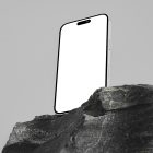 Seen from below, the blank iPhone 14 Pro Mockup standing on the big rock against the gray wall in the background.