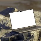 Front view, space gray blank MacBook Pro Mockup standing on the sunny rocks on the beach against water in the background.