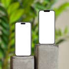 Front view, two blank iPhone 14 Pro Mockups standing on the square piece of concrete against monstera flowers and beige wall.