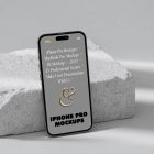 Front view iPhone 14 Pro Mockup with gray design based on the piece of a styrofoam and standing on the white floor against white wall.