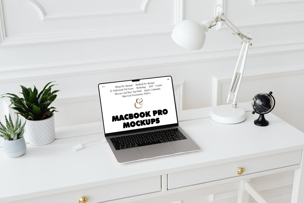 Front view MacBook Pro Mockups with white design laying on the white wooden desk with gold elements, with a white desk lamp, flowers, and black mini globe. Everything is against a white wall.