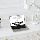 Front view MacBook Pro Mockups with white design laying on the white wooden desk with gold elements, with a white desk lamp, flowers, and black mini globe. Everything is against a white wall.