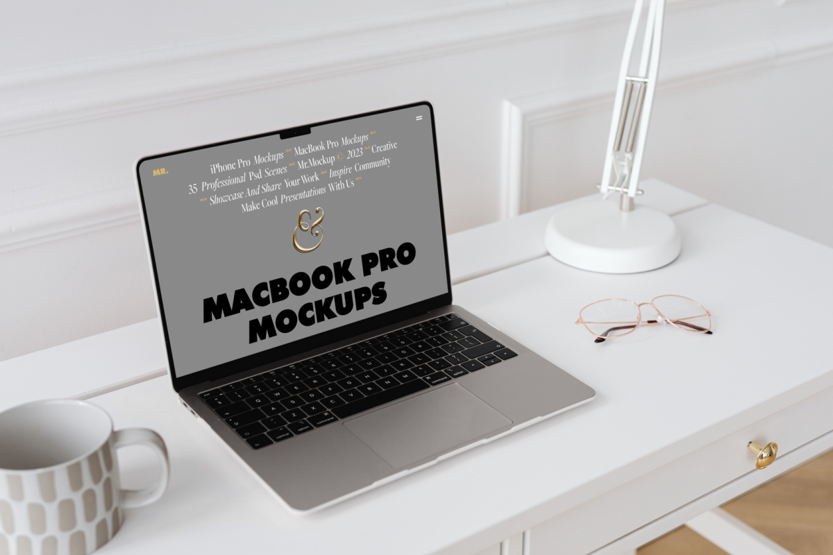 Front view MacBook Pro Mockups with gray design laying on the white wooden desk with gold elements, with a white desk lamp and white cup, everything is against a white wall.
