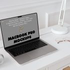 Front view MacBook Pro Mockups with gray design laying on the white wooden desk with gold elements, with a white desk lamp and white cup, everything is against a white wall.