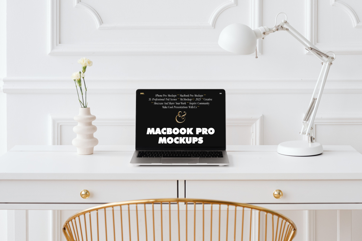 Front view MacBook Pro Mockups with black design laying on the white wooden desk with gold elements, with a white desk lamp and modern vase. Before the white desk standing gold desk chair. Everything is against a white wall.