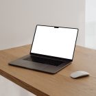 Front view, blank MacBook Pro Device Mockups laying on the wooden desk, white apple mouse against white walls in the flat.