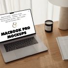 Front view MacBook Pro Mockups with white design laying on the wooden desk with a candle, magazine, and modern desk lamp against a white curtain.