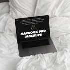 Front view MacBook Pro Mockups with black design laying on the white linen on bed.