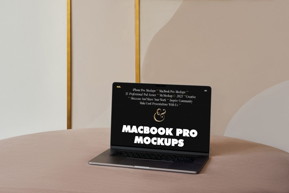 Front view MacBook Pro Mockups with black design laying on the beige table against the wall with white, gold and beige decoration in the background.