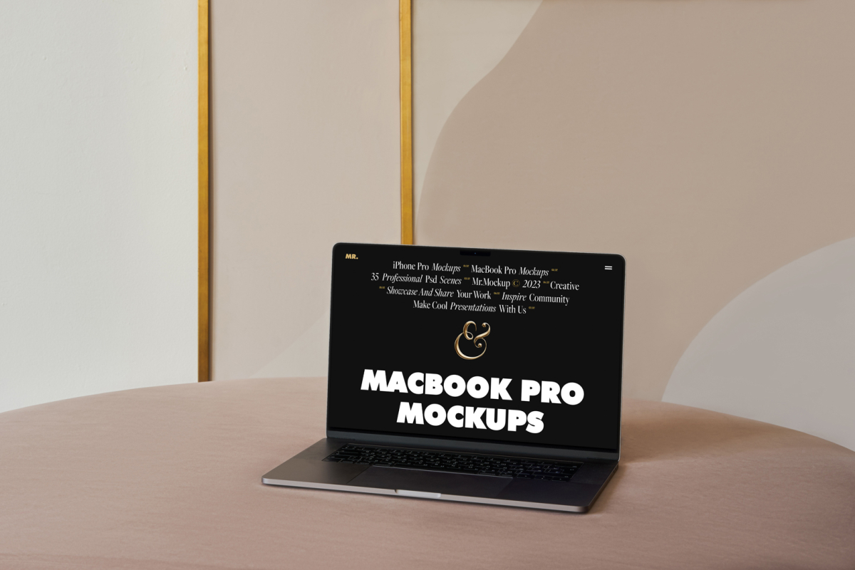 Front view MacBook Pro Mockups with black design laying on the beige table against the wall with white, gold and beige decoration in the background.